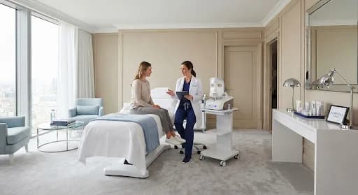 Aesthetic practitioner with a tablet talking with a woman seated on a treatment bed in a bright suite